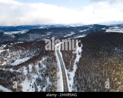 Drone-Bild mit hoher Neigung von oben nach unten auf der Straße Durch die Bäume und Wald in Bergkette mit bedeckt Weißer Schnee am Wintertag in der Nähe von Knjazevac Stockfoto
