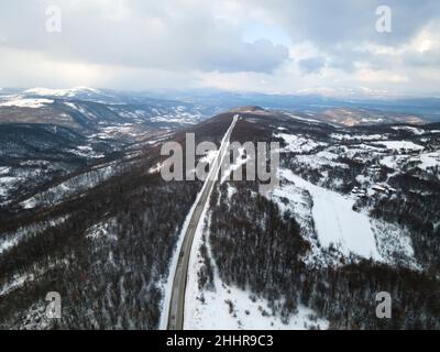 Drone-Bild mit hoher Neigung von oben nach unten auf der Straße Durch die Bäume und Wald in Bergkette mit bedeckt Weißer Schnee am Wintertag in der Nähe von Knjazevac Stockfoto