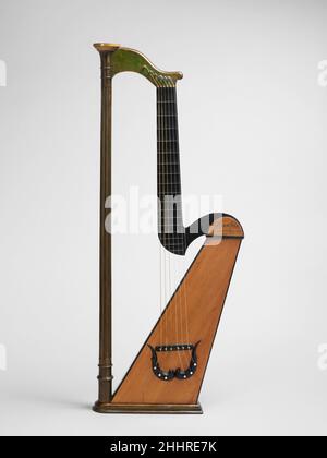 Harp Guitar 1827 Joseph Laurent Mast French Dieses ungewöhnliche Instrument hat sechs Einzelsaiten wie eine Gitarre, aber mehrere Körpermerkmale wie eine Harfe. Das ungewöhnliche Fichtensoundboard erinnert an das einer Harfe, zeigt aber nach vorne und ist parallel zu den Saiten, anstatt senkrecht zu den Saiten zu sitzen wie auf einer Pedalharfe. Hinter dem Resonanzboden befindet sich ein zylindrischer Korpus aus gebogenem Ahorn. Der Körper ist grün gefärbt und hat zwei ovale Schalllöcher. Das breite, untere Ende des Körpers ruht auf einer flachen Platte, auf der das Instrument eigenständig stehen kann. Die harfenähnliche Säule misst 88,5 cm in der Höhe und Stockfoto