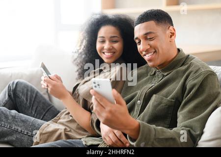 Multirassisches Paar mit Smartphone auf der Couch und Freizeit in sozialen Netzwerken. Frau, die mit ihrem Freund auf der Couch sitzt Stockfoto