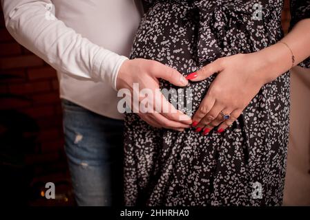Konzept von Schwangerschaft und Mutterschaft, Einheit der Familie. Eine schöne Schwangerin hält den Bauch von unten und oben. Sie legt ihre Hände an Stockfoto