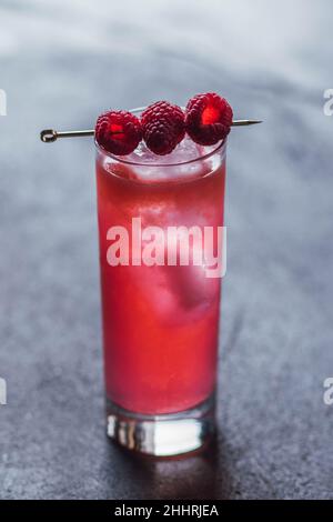 Hoher rosafarbener Cocktail-Drink mit drei Himbeeren auf Cocktail-Pick, auf Beton Stockfoto