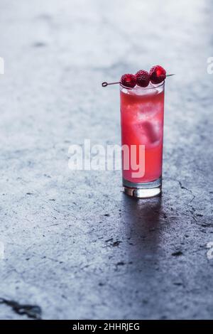 Hoher rosafarbener Cocktail-Drink mit drei Himbeeren auf Cocktail-Pick, auf Beton Stockfoto