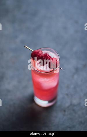 Hoher rosafarbener Cocktail-Drink mit drei Himbeeren auf Cocktail-Pick, auf Beton Stockfoto