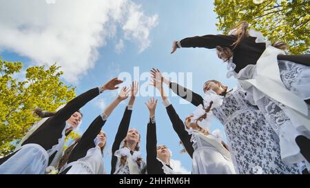 Glückliche russische Schulabgänger strecken sich an ihrem letzten Schultag die Hände. Stockfoto