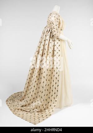 Abendkleid 1797–99 Britisch Dieses schöne Kleid zeigt die feine Handwerkskunst und Textilien, die Ende des 18th. Jahrhunderts verwendet wurden, um sich mit der übertriebenen Mode der hohen Taille, der großen Kopfbedeckungen und der spitz zulaufenden Silhouetten zu koordinieren. Die Empire-Silhouette lässt sich leicht mit ihrem Ursprung im Chiton der antiken Greco-Römer identifizieren, einem röhrenförmigen Gewand, das von den Schultern drapiert und manchmal unter der Büste gegurtet wurde. Im Laufe der Kostümgeschichte wurden mehrere Neuinterpretationen durchgeführt, aber keine davon war so bemerkenswert wie die Zeit, die die rechteckigen, panierroten Röcke der 18t überbrückt Stockfoto