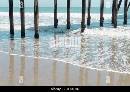 Pier Pilings reflektiert auf einem nassen Sandstrand und Wellen in San Simeon, Kalifornien Stockfoto