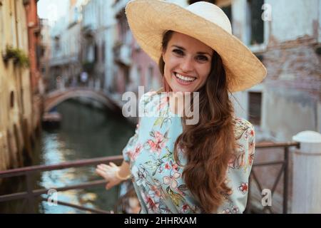 Glückliche elegante Frau in Blumenkleid mit Hut Sightseeing in Venedig, Italien. Stockfoto