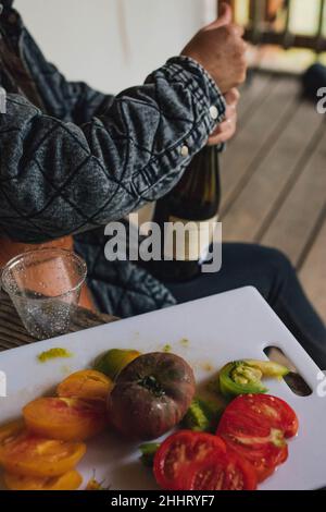 Frau öffnet eine Flasche Wein neben dem Schneidebrett mit Tomaten aus Erbstück Stockfoto