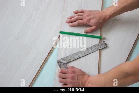 Die Hände der Arbeiter installieren einen Holzlaminatboden. Renovierung des Hauses mit Holzböden mit Maßen. Stockfoto