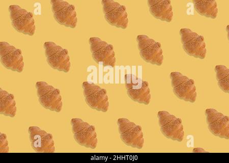 Kreatives Muster aus frisch gebackenen Croissants auf hellgelbem Hintergrund. Minimaler Ansatz für Backwaren. Stockfoto
