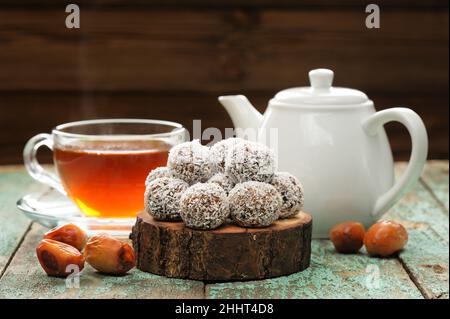 Hausgemachte vegane Süßigkeiten in Kokosnussspelzen serviert mit dampfendem heißen schwarzen Tee horizontal Stockfoto