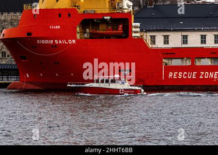 Das Rote Kreuz-SAR-Schiff Hordaland Røde Kors verlässt den Binnenhafen von Bergen, Norwegen. Vorbei an einem Offshore-Versorgungsschiff in Festningskaien Stockfoto