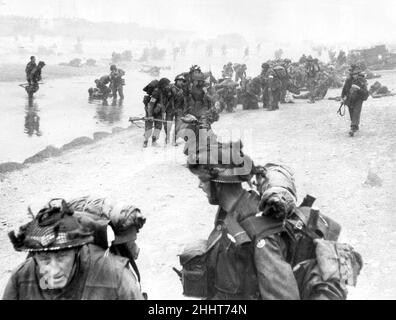 Truppen der 3rd Infantry Division landen am Queen Red Beach, Sword Area, Anfang des 6th. Juni 1944, der ersten britischen Formation, die am Sword Beach landet. Im Vordergrund befinden sich die Sapper von 84 Field Company Royal Engineers, die zur No.5 Beach Group gehören, die durch die weißen Bänder um ihre Helme gekennzeichnet sind. Hinter ihnen sind medizinische Anorderungen von 8 Field Ambulance, RAMC, zu sehen, die verwundete Männer unterstützen. Im Hintergrund sind Kommandos der 1st Special Service Brigade zu sehen, die von ihrem LCI(S) Landungsschiff aussteigen. 6th. Juni 1944 Stockfoto