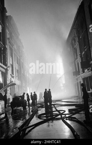 Feuerwehrleute des Hilfsfeuerwehrdienstes besuchen den Schauplatz eines brennenden Gebäudes in der Nähe von Piccadilly, Central London, nachdem bei einem Angriff der deutschen Luftwaffe auf London hochexplosive Bomben abgeworfen wurden.14th. Oktober 1940. Stockfoto