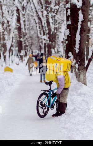 Krasnodar, Russland - 24 2022. Januar: Kurier, ein Lebensmittellieferer mit einem Thermobeutel auf dem Rücken, der ein Fahrrad repariert Stockfoto