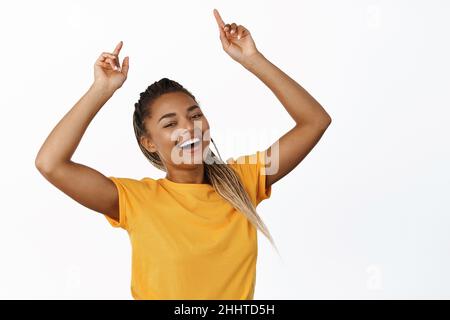 Bild einer lächelnden schwarzen Frau, die mit den Fingern nach oben zeigt, große Werbung, Verkaufswerbung, gelbes T-Shirt, weißer Hintergrund Stockfoto