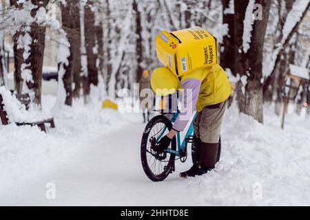 Krasnodar, Russland - 24 2022. Januar: Kurier, ein Lebensmittellieferer mit einem Thermobeutel auf dem Rücken, der ein Fahrrad repariert Stockfoto