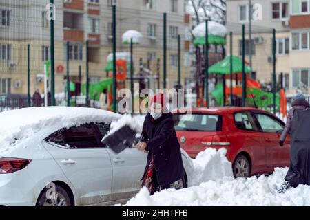 Krasnodar, Russland - Januar 24 2022: Ältere Frau entfernt Schnee mit einer Schaufel. Schaufelende Straße von fallendem Schnee Stockfoto