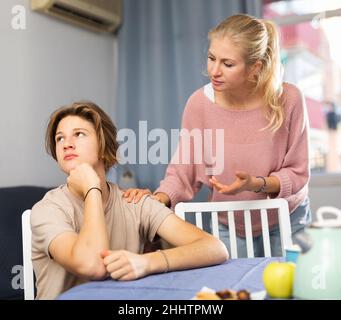 Unruhigen Teenager Junge zu Hause sitzen, während seine Mutter ihn schimpft Stockfoto