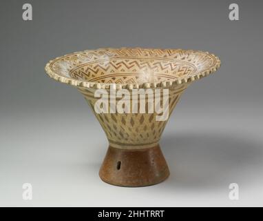 Podest Bowl 6th–8th Century Moche Diese ausgestellte Schale, genannt Florero, hat einen leeren Podest-Sockel, der mit kleinen Keramikpellets gefüllt ist, die beim Schütteln des Gefäßes klappern. Moche ausgestellte Schalen wurden ab dem vierten Jahrhundert A.D. hergestellt.Sie wurden im Laufe der Zeit größer, mit kleineren Basen und breiteren, everted Felgen. Die komplexe Dekoration ist fast ausnahmslos im Inneren des Randes lackiert, während das Äußere des Schiffes einfachere Designs zeigt. Diese ausgestellte Schale ist mit einem Netzmotiv auf der Außenseite und mit ineinander verschränkenden Zickzacklinien mit Dreiecken auf der Innenseite verziert. Die geometrische Dekoration, sowie Th Stockfoto
