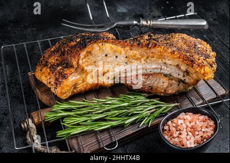 Gegrilltes Schweinefleischbauch auf einem Grill mit Rosmarin. Schwarzer Hintergrund. Draufsicht Stockfoto