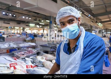 Selektive Konzentration auf das freundliche, fröhliche Gesicht eines hübschen jungen erwachsenen Fischers aus dem Nahen Osten, der Maske trägt und frischen Fisch auf dem traditionellen Fischmarkt verkauft. Stockfoto