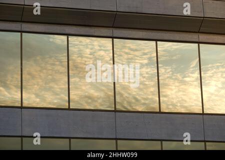 Verträumte weiße Wolken und Himmel spiegeln sich in den Fenstern eines modernen Bürogebäudes aus Beton wider Stockfoto