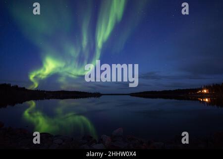 Helle Aurora Borealis (Nordlichter), die sich in der Dämmerung im See und über der Hütte spiegeln, Northwest Territories, Canada Stockfoto