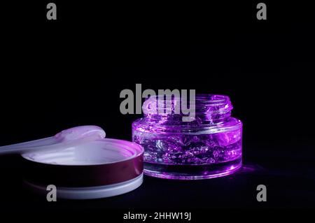 Transparentes Glas mit violettem feuchtigkeitsspendenden Gel-Licht auf schwarzem Hintergrund Stockfoto