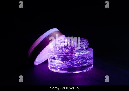 Transparentes Glas mit violettem feuchtigkeitsspendenden Gel-Licht auf schwarzem Hintergrund Stockfoto