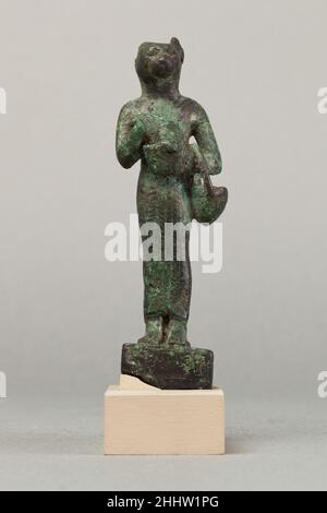 Bastet mit Löwenkopf-Aegis und Korb 664–30 v. Chr. späte Periode–ptolemäische Periode Bastet, hier als katzenköpfige Göttin dargestellt, war eine mächtige Schutzfigur, die auch für ihre Fruchtbarkeit bekannt war. Sie konnte auch mit einem Löwenkopf dargestellt werden, aber als katzenköpfige Göttin wurden ihre friedlichen Züge betont. Ihre persönlichen Verzierungen und Kleidungsstücke sind auf Statuetten ausgefeilt, oft mehr als andere Göttinnen, und sie trägt in der Regel zahlreiche Attribute. Diese Figur hält eine schützende Löwenkopf-Aegis und hielt wahrscheinlich einmal ein Sirum in ihrer anderen Hand. Sie trägt einen Korb auf ihrem anderen Arm. Stockfoto