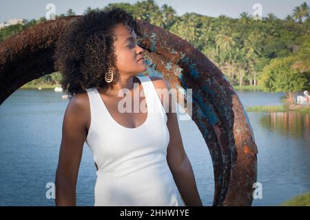 Schönes Model in einem weißen Kleid lächelnd und schauend auf die Kamera. Im Hintergrund Bäume, Pflanzen, Blumen und der Fluss in der Landschaft. Salvador Stockfoto