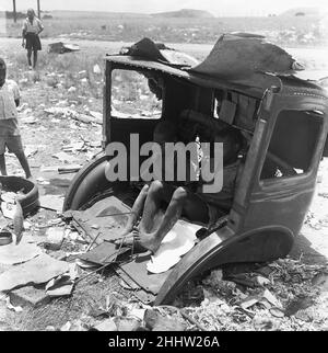 Kinder aus den Townships Langa und Windermere sahen hier, wie sie die Müllkippe von Orlando in der Nähe von Kapstadt durchdrangen. Zwei kleine Jungen suchen Schatten von der Mittagssonne in einem Autowrack am 4th. Februar 1955 Stockfoto