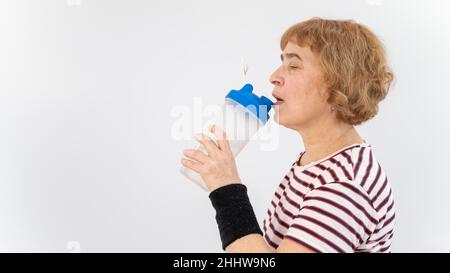 Ältere Frau trinkt Wasser, während sie auf weißem Hintergrund trainiert. Stockfoto