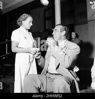 Primo Carnera, Schauspieler und professioneller Wrestler, ebenfalls ein ehemaliger Profiboxer, fotografiert während der Pause von Drehszenen für den neuen Film A Kid for Two Farthings, in den Shepperton Studios, Surrey, England, 13th. September 1954. Das Set ist eine Darstellung eines Wrestling-Rings in East London. Er spielt Python Macklin. Stockfoto