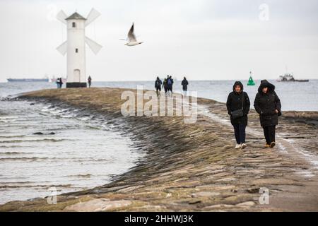 Die Menschen sahen, wie sie um das Stawa Mlyny-Leuchtfeuer am Eingang zum Hafen von Swinoujscie gingen. Ein weißes Leuchtfeuer in Form einer Windmühle ist ein Symbol von Swinoujscie und ist Teil des offiziellen Logos der Stadt. Der Hafen von Swinoujscie ist ein polnischer Seehafen an der Ostsee. Zusammen mit dem Hafen von Stettin entsteht einer der größten Hafenkomplexe an der Ostsee. Stockfoto