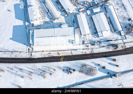 Luftaufnahme von oben auf schneebedeckte Lagergebäude und Lagerhäuser in einem Industriegebiet an sonnigen Wintertagen Stockfoto