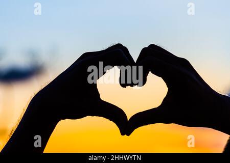 Liebeszeichen. Herz-Symbol von Hand Silhouette in Sonnenuntergang Himmel. Hintergrund im Vintage-Stil Stockfoto