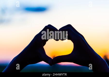 Liebeszeichen. Herz-Symbol von Hand Silhouette in Sonnenuntergang Himmel. Hintergrund im Vintage-Stil Stockfoto