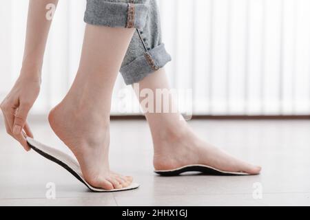 Frau, die orthopädische Innensohle innen anpasst, Nahaufnahme. Mädchen, das zu Hause eine Innensohle neben dem Fuß hält. Orthopädische Einlagen. Banner zur Fußpflege. Flache Füße Stockfoto