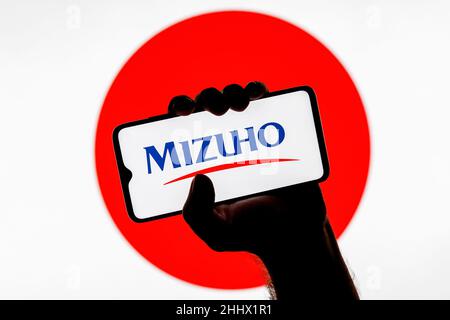 Smartphone mit Mizuho Financial Group Logo auf dem Bildschirm in geballter Hand auf dem Hintergrund der Japan-Flagge Stockfoto