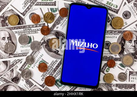 Smartphone mit dem Logo der Mizuho Financial Group, umgeben von verschiedenen Metallmünzen auf dem Hintergrund von Dollarscheinen Stockfoto