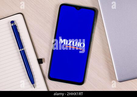 Smartphone mit Mizuho Financial Group Logo auf Holztisch neben Laptop und Business-Planer Stockfoto