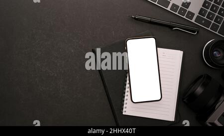 Minimalistisch moderner schwarzer Schreibtisch mit Arbeitsgeräten, Smartphone leerer Bildschirm-Mockup für Ihre Grafik- und Kopierfläche auf schwarzem Hintergrund. Flaches Lay, t Stockfoto
