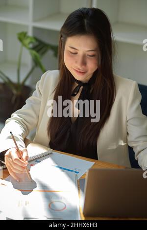Das Porträt einer glücklichen asiatischen Geschäftsfrau konzentriert sich im Büro auf ihre Marketingberichte. Eine Arbeitnehmerin, die mit dem Bericht arbeitet. Stockfoto