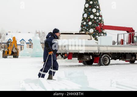 Ein Mann in einer blauen Jacke und einem schwarzen Strickmütze trägt Eisplatten auf einem Holzschlitten Stockfoto