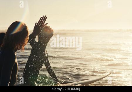 Halten Sie die Stimmung in Gang. Aufnahme einer Gruppe junger Surfer, die gemeinsam im Meer surfen. Stockfoto