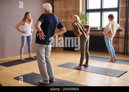 Junge Trainerin und eine Gruppe älterer Menschen, die während des Sporttrainings auf Matten stehen und körperliche Übungen machen Stockfoto