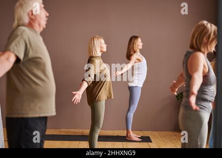 Ältere Menschen wiederholen körperliche Übungen, nachdem eine junge Fitnesslehrerin auf einer Matte auf dem Holzboden stand Stockfoto